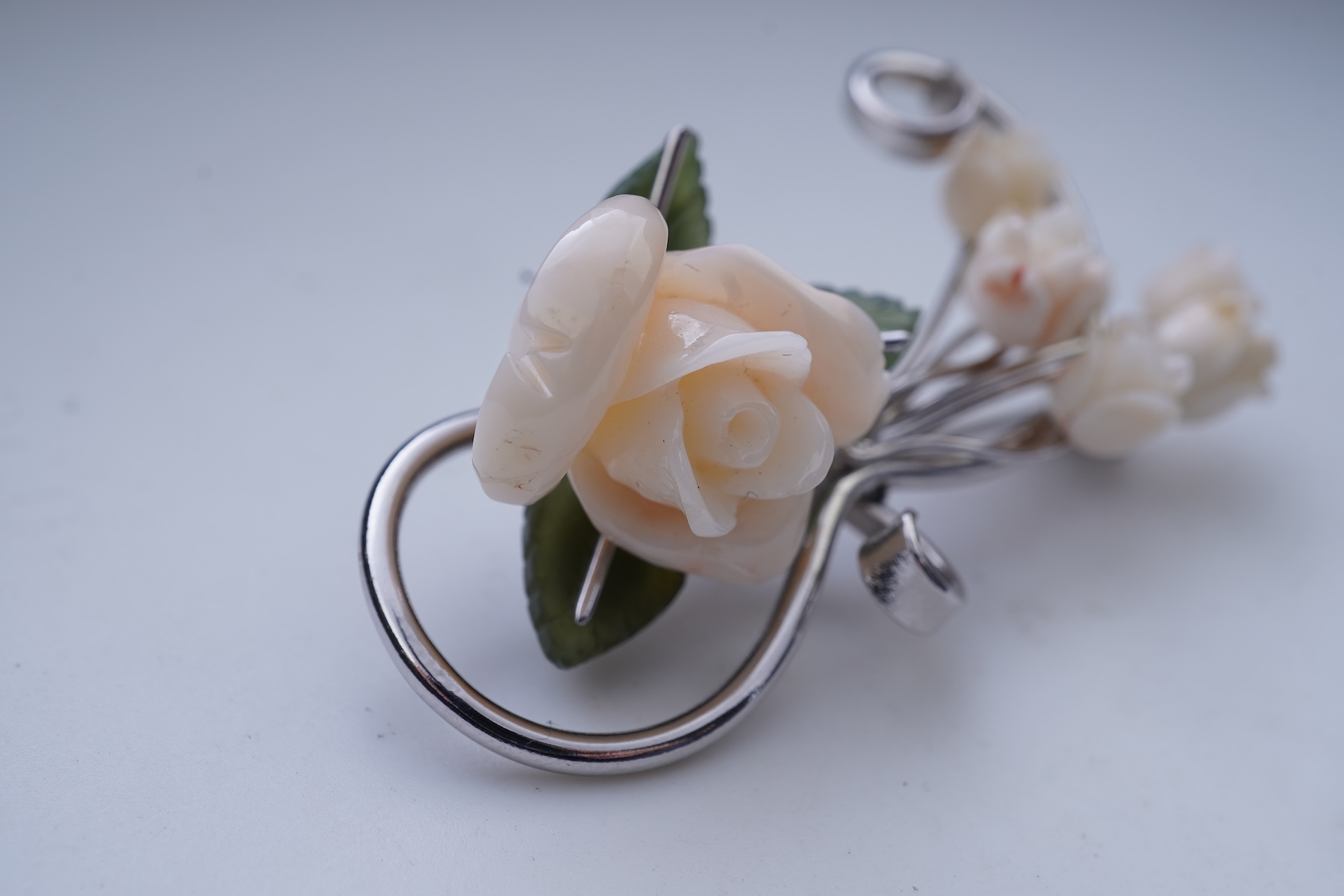 A white coral and nephrite brooch, designed as a spray of roses in carved white coral with nephrite leaves, on a scrolled white gold mount, length 5.5cm, stamped 14K, gross weight 11 grams